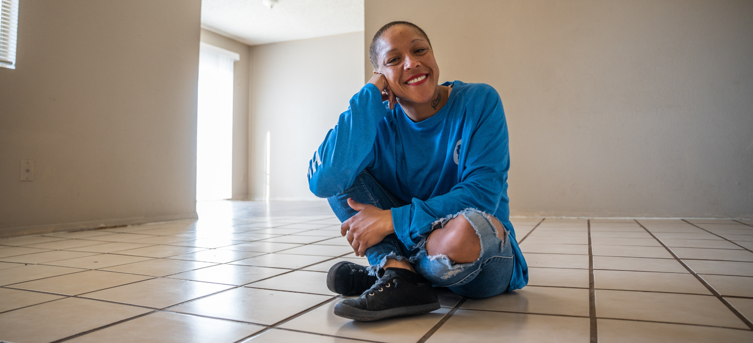 Woman sitting on the floor in an empty room smiling at the camera