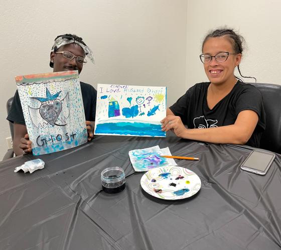 A man and a woman smiling holding up their paintings