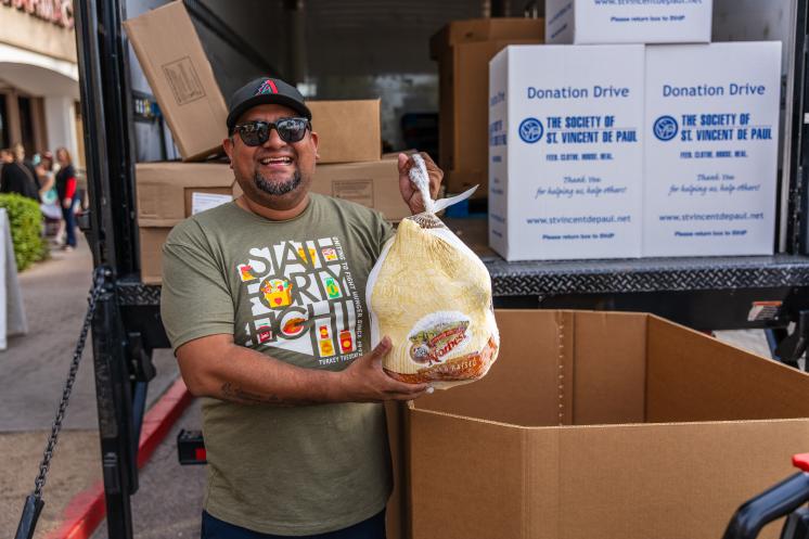 Man standing next to a box holding a turkey and smiling