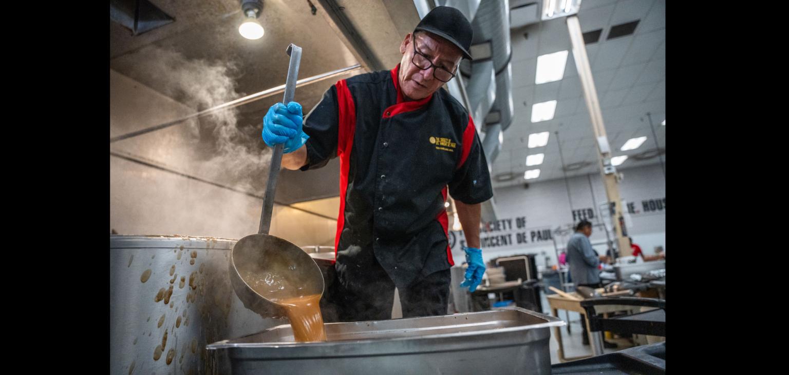 Mike ladles gravy into a tray of Turkey for Thanksgiving meals.