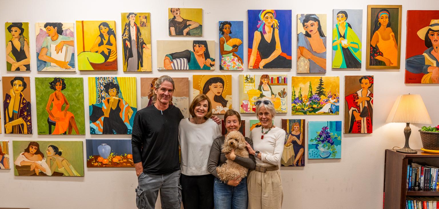 Most of the team behind the painting-donation project stands before a wall covered in paintings.