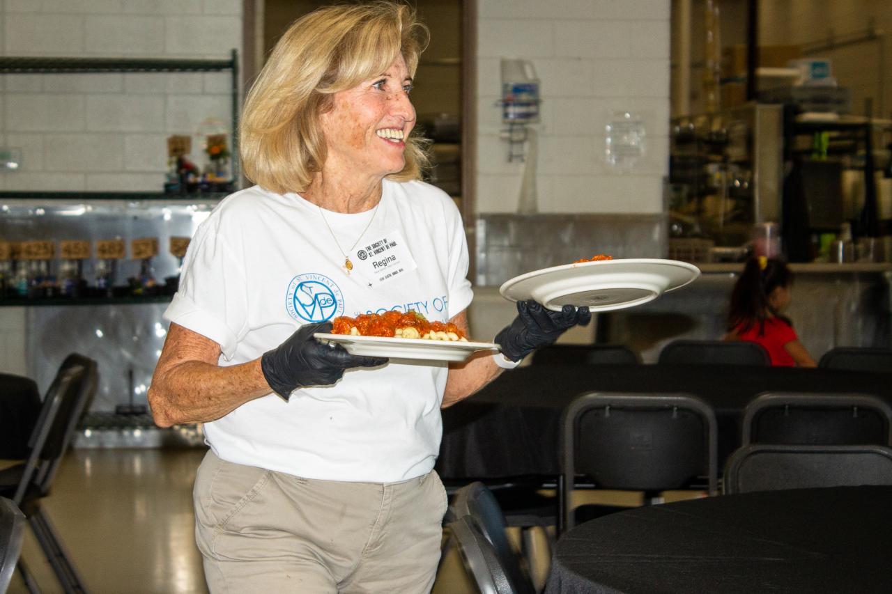 Regina meyers carrying plates of food and serving meals in the SVdP Family Dining Room